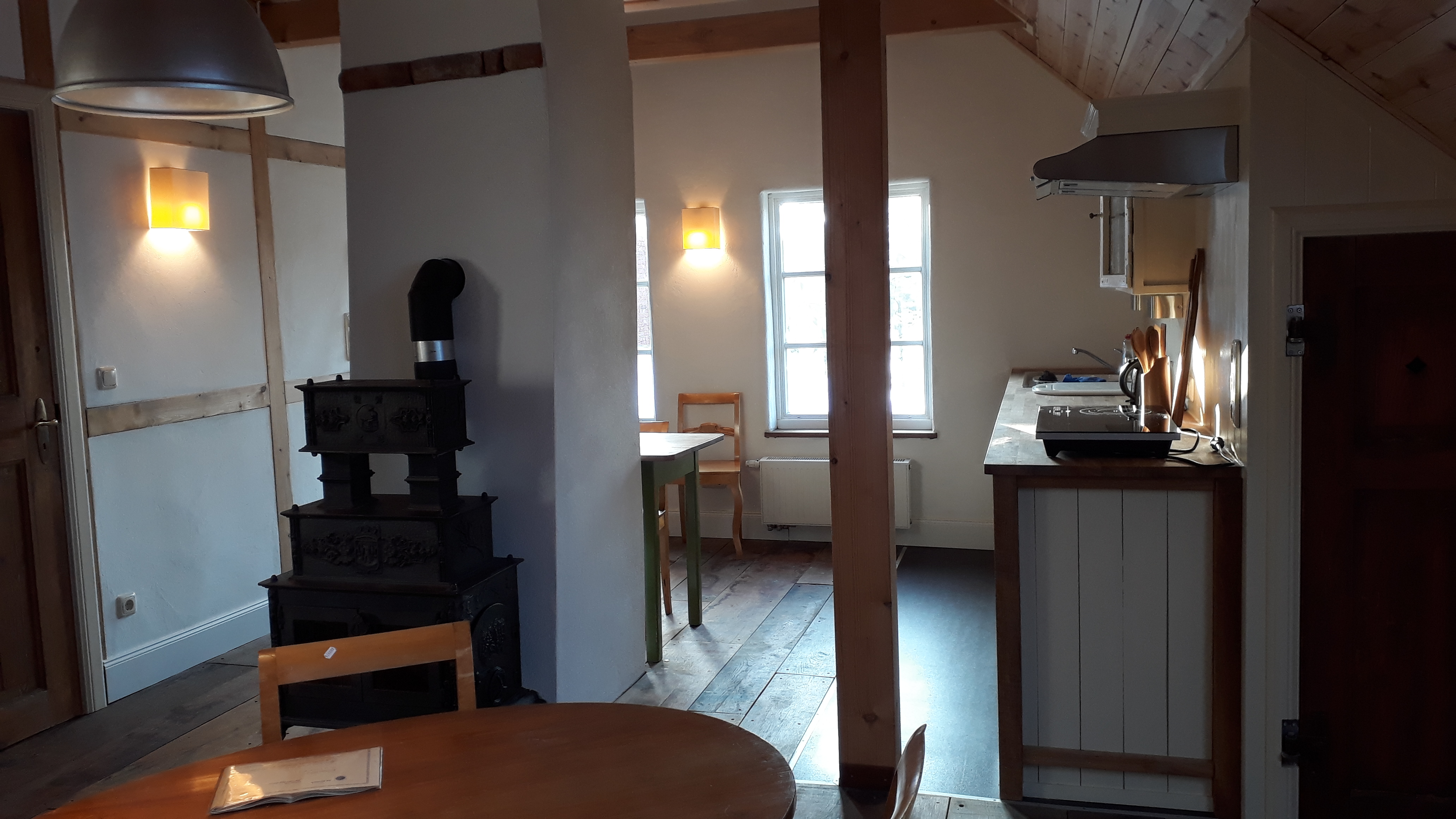Blick aus dem Wohnbereich in den Kochbereich. Der schmiede-eiserne Ofen ist zu sehen.